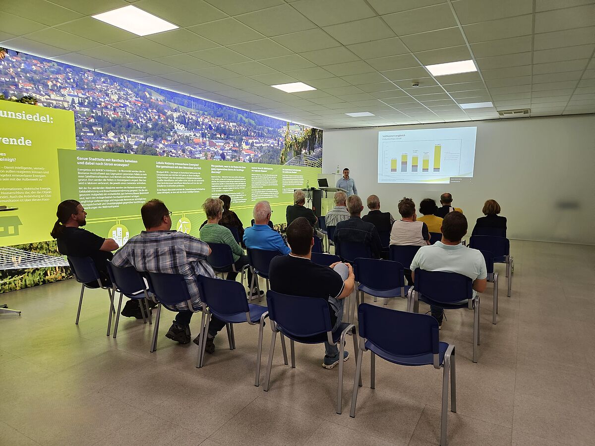 Mehrere Personen sitzen auf Stühlen in einem Konferenzsaal und lauschen einem Vortrag der SWW- Auf der Leinwand vorne ist ein Säulendiagramm zu sehen.